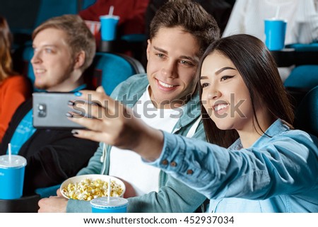 Taking a pic. Shot of a beautiful multicultural young loving couple taking a selfie at the cinema