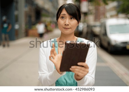 Young Asian woman in city using tablet computer walking