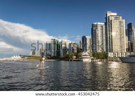 Tourist exploring Coal Harbour on a paddle board. Picture taken in Downtown Vancouver, BC, Canada, on a cloudy evening before sunset.