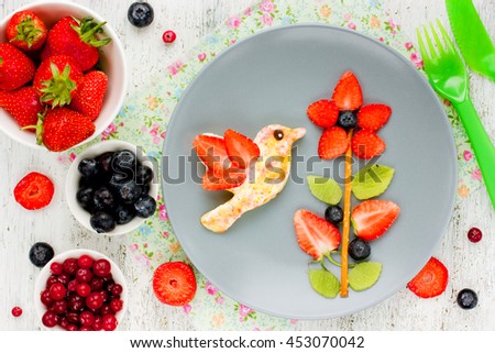 Creative idea for the kid's breakfast or dessert - flower of fresh strawberries kiwi and blueberries and toast with butter and sugar shaped bird hummingbird. Cute summer food, edible picture on plate