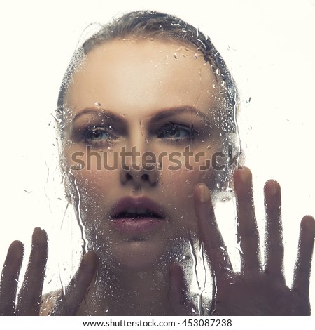 Beauty face of young caucasian woman near a mirror with water drops. Studio portrait. Isolated on white background. Toned