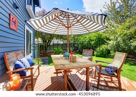 Wooden walkout deck in the backyard garden of blue siding house. Furnished with patio table set with umbrella