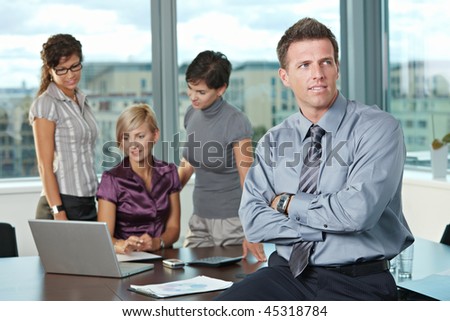 Confident businessman at office with business team in background.