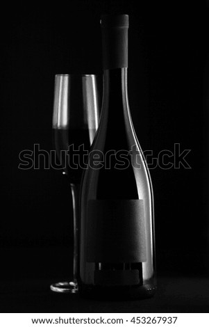 Elegant red wine glass and a wine bottle in black background
