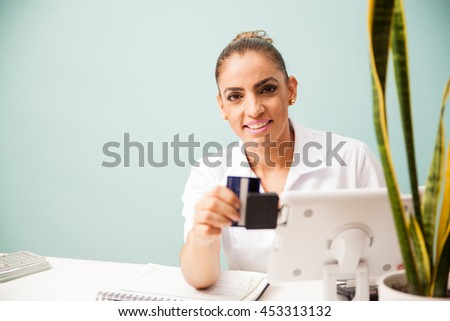 Therapist and business owner swiping a credit card and smiling while sitting in a front desk at a spa