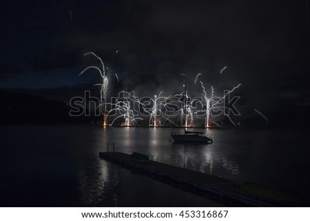 Ignis Brunensis silver and gold colored fireworks resembling aster flower reflecting on water surface of dam. Long exposure night graphical photography using creative tilt effect by tilt-shift lens.