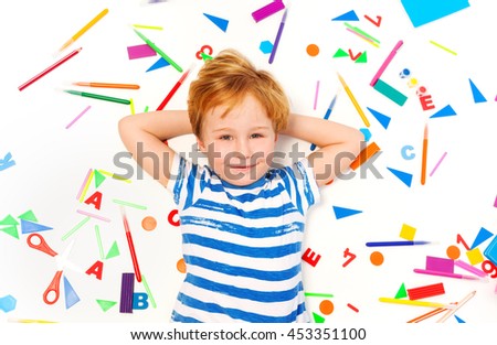 Kid laying among heap of school office supplies