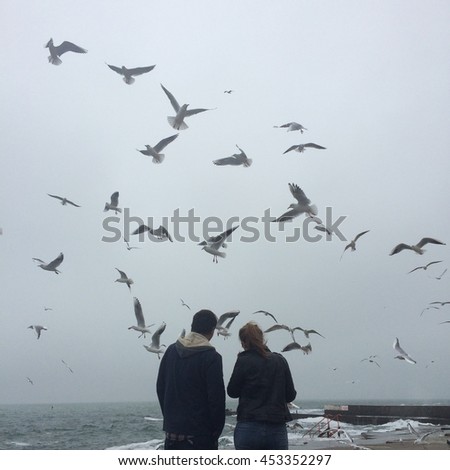 Couple standing at pier,seagulls.people and birds, seascape,stormy sea Royalty-Free Stock Photo #453352297