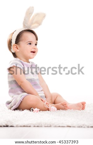 Happy baby girl in easter costume sitting on carpet, laughing. Isolated on white background.