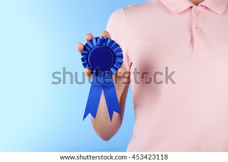 Woman holding blue award prize ribbon on color background