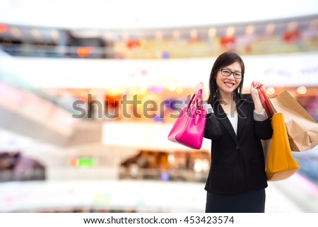 Happy young woman with shopping bags over bokehl shopping mall background