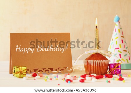 Birthday concept with cupcake and candle next to greeting card on wooden table