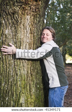 A colour portrait photo of a happy smiling forties man hugging a tree in the forest.