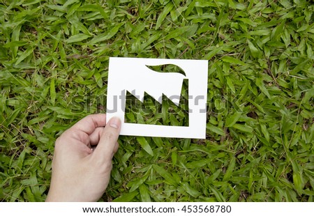 Hand holding paper cut in factory shape on green grass.Eco friendly green living