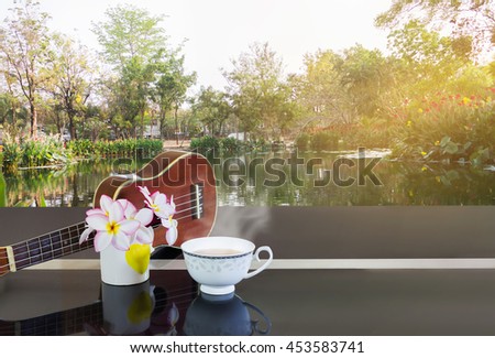 Cup of hot tea or hot drink with flowers and ukulele with happy morning green fresh garden and pond view background