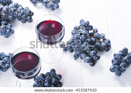 two glasses of red wine and blue grapes on white wooden table background