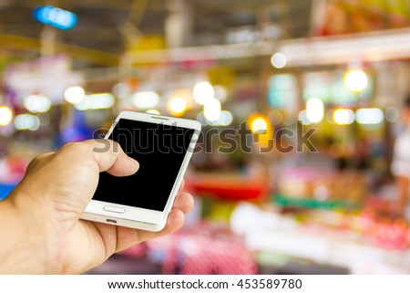 Man use mobile phone, blur image of rural market as background.