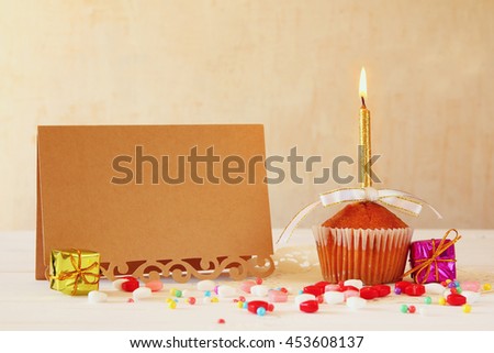 Birthday concept with cupcake and candle next to empty greeting card on wooden table