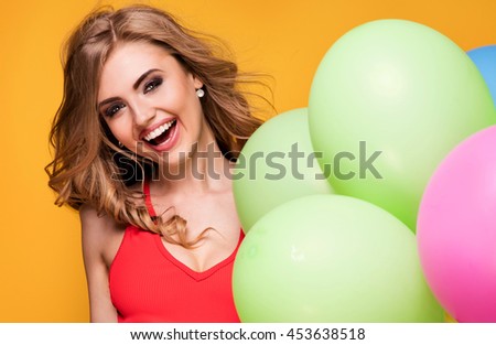 Young pretty blonde woman posing with colorful balloons. Yellow background. Studio shot. Happiness content. Toothy smile.