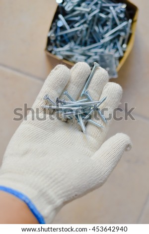 Closeup photo on person hand in glove holding screws, light background