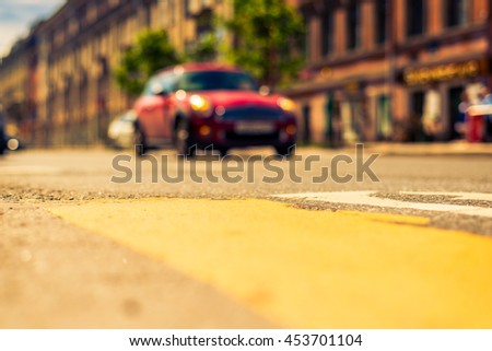 Sunny day in the big city, red car racing on road. View from the pedestrian crossing, focus on the asphalt, image in the yellow-blue toning