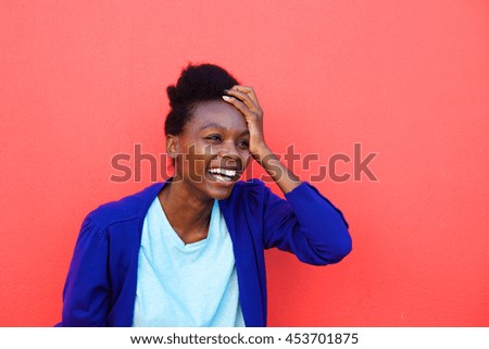 Portrait of excited young african woman laughing with her hand on head against red background