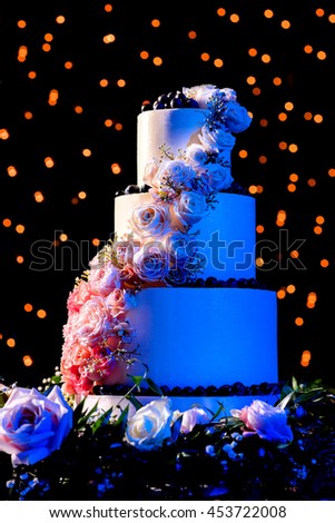 Picture of a beautiful wedding cake with roses and blue lighting with bokeh background.