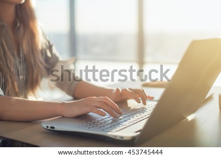 Female writer typing using laptop keyboard at her workplace in the morning. Woman writing blogs online, side view close-up picture