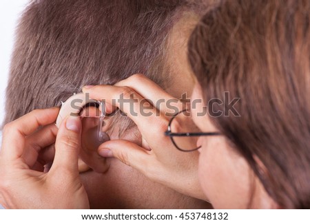 Doctor inserting a hearing aid in an ear of a senior man
