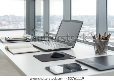Workplace with notebook laptop Comfortable work table in office with windows and city view Royalty-Free Stock Photo #453761119
