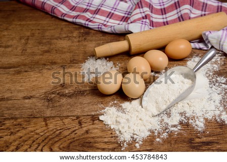 Flour, eggs, salt, towel, rolling pin on wooden table ready for cooking