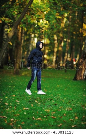 A wonderful picture with depth and volume, creating a deceptive effect that a young serious man in a jacket with a hood, as if, goes high above the grass in the air in autumn Park.