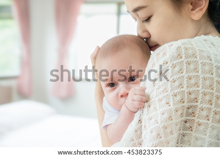 Picture of happy Asian mother kiss infant baby boy after cry. Closeup at mother and infant baby.