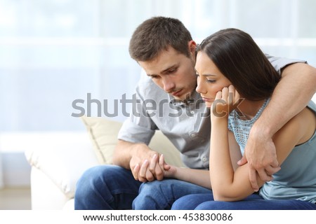 Sad couple comforting each other sitting on a couch in the living room at home Royalty-Free Stock Photo #453830086