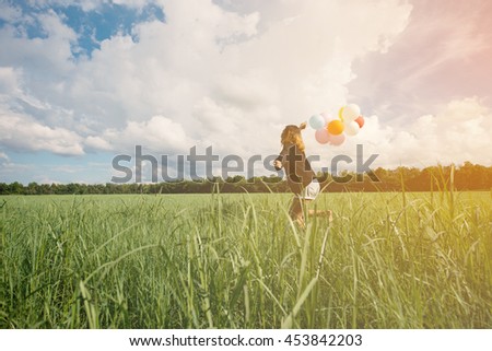 Girl running on the field with balloons at sunrise. Happy woman on meadow.