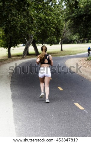 Caucasian Teen Woman Running On Bike Path Away From Camera Pony Tail Black Top White Shorts