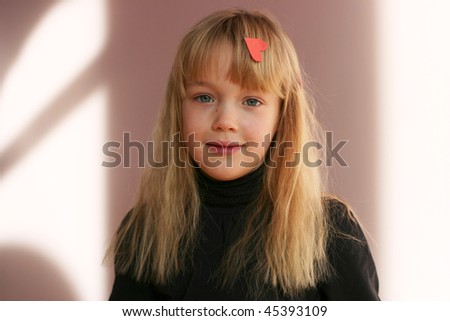 Pretty blonde little  smiling girl with heart in her hair on pink background