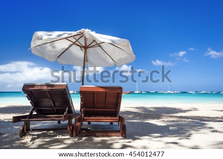 Sun umbrella and sunlongers on sandy tropical beach with white sand and turquoise sea water Royalty-Free Stock Photo #454012477
