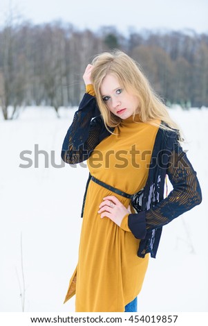 Young attractive girl in yellow dress posing on winter snowy glade