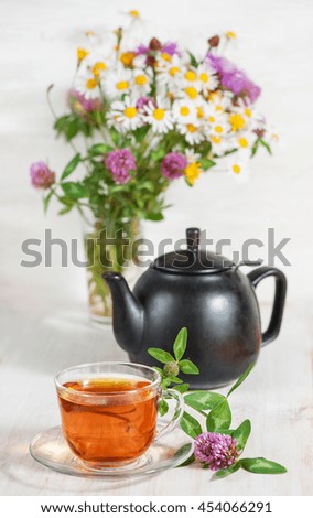 Cup of tea, teapot and branch of clover on wooden background