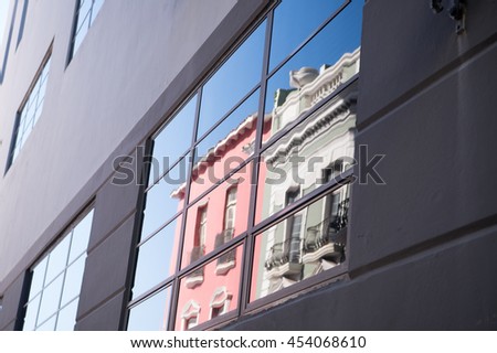 glassy background of building grey concrete wall with reflected glass on window reflecting blue sky and houses outdoor