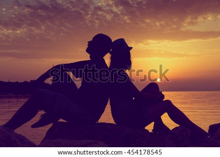 Couple in love sitting on the rocks near the sea, on their summer vacation, enjoying a beautiful sunset