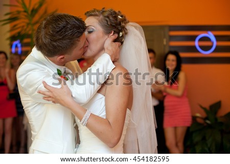 A passionate kiss between newlyweds standing in an orange dance hall
