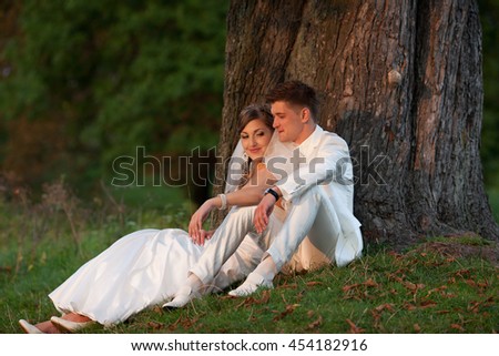 Happy wedding couple sits at the old tree