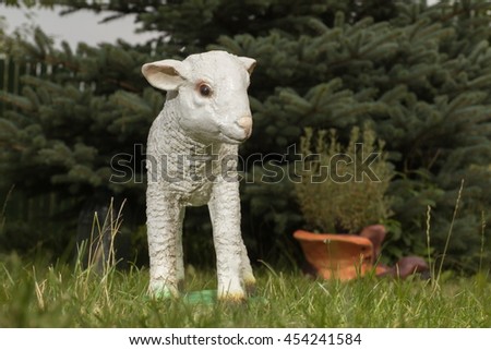 White ceramic plaster statuette of a lamb, sheep on the grass.