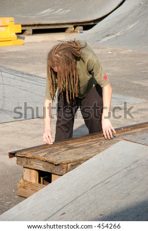 Male teen skateboarder with dreadlocks waxing rail at skate park.