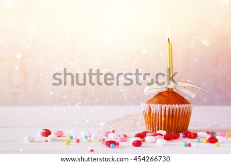 Birthday concept with cupcake and candle on wooden table. Glitter overlay