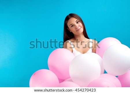 Portrait of lovely brunette girl with pink balloons looking at camera on blue background.Studio shot.