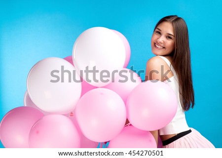 Side view of pretty young girl with air balloons posing at camera on blue background