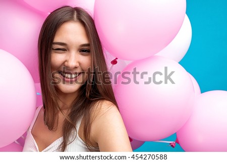 Close-up of pretty young girl winking at camera while taking self-portrait in pink balloons